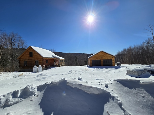 yard covered in snow with a garage, a wooded view, and an outdoor structure