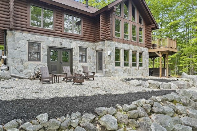 back of property featuring a deck, a fire pit, stone siding, and log exterior