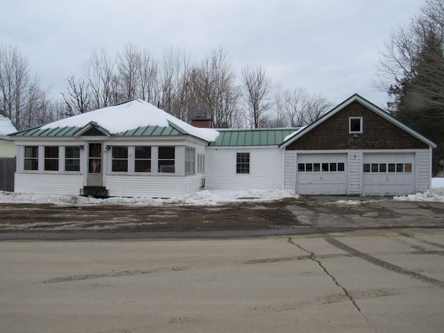 view of front of property featuring a garage, metal roof, a standing seam roof, and driveway