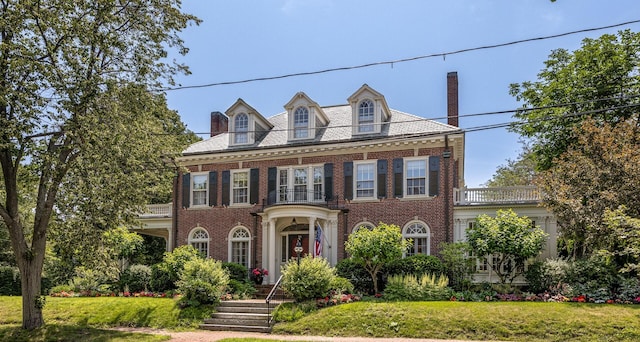 colonial home featuring a balcony, a front lawn, and brick siding