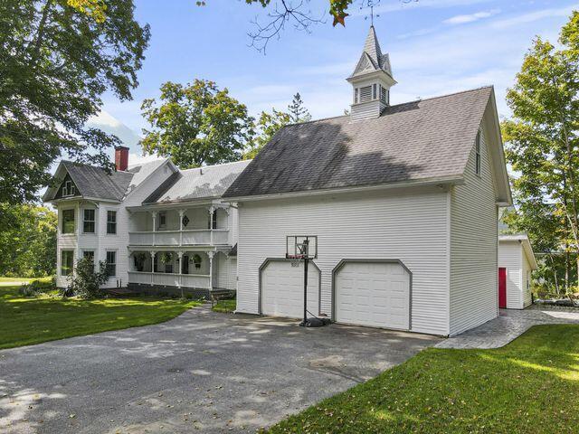 rear view of property featuring a garage, a balcony, driveway, and a lawn