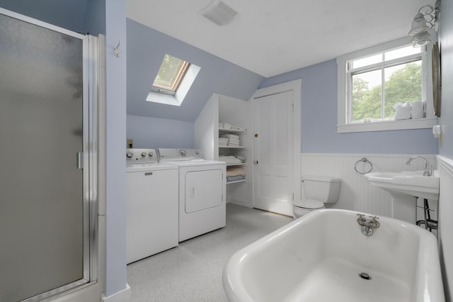 bathroom with a freestanding tub, a wainscoted wall, separate washer and dryer, a shower stall, and lofted ceiling with skylight