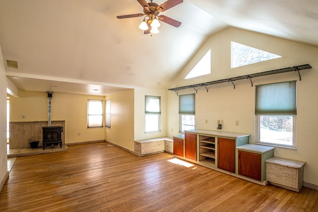 living area with baseboards, ceiling fan, a wood stove, light wood-style floors, and high vaulted ceiling