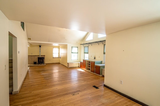 unfurnished living room featuring visible vents, light wood-style flooring, a wood stove, vaulted ceiling, and baseboards