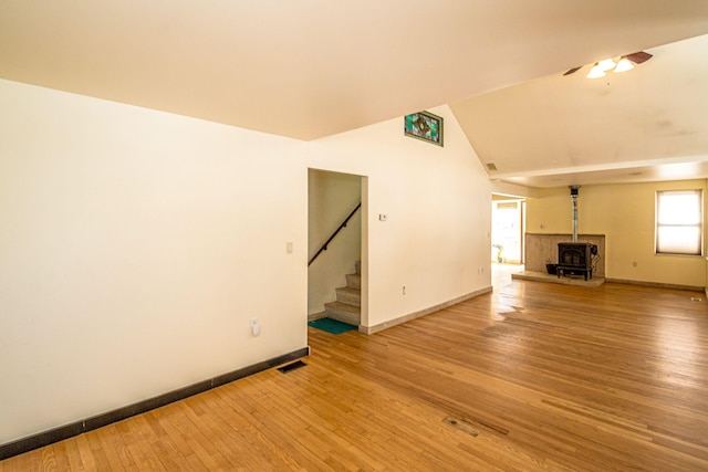 unfurnished living room with wood finished floors, visible vents, baseboards, stairs, and a wood stove