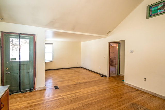 foyer entrance with light wood finished floors, visible vents, baseboards, and high vaulted ceiling