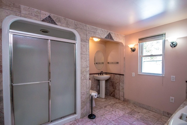 full bathroom featuring a sink, marble finish floor, a shower stall, and tile walls