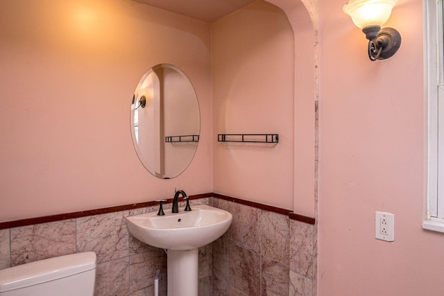 half bathroom featuring toilet, a sink, tile walls, and wainscoting