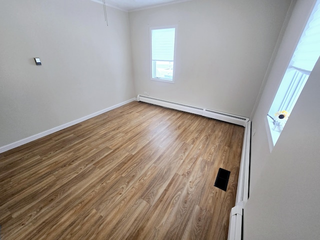 unfurnished room featuring a baseboard heating unit, wood finished floors, and baseboards