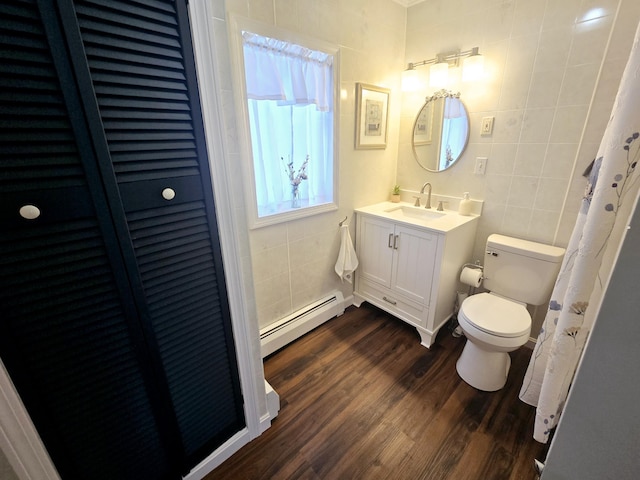 full bath featuring toilet, a closet, baseboard heating, and tile walls