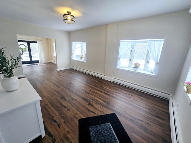 unfurnished living room with a baseboard heating unit, dark wood-type flooring, and baseboards