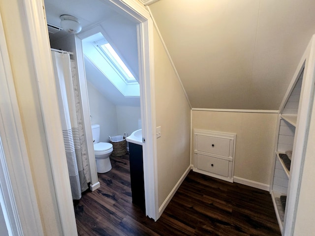 bathroom featuring vaulted ceiling with skylight, baseboards, toilet, wood finished floors, and curtained shower