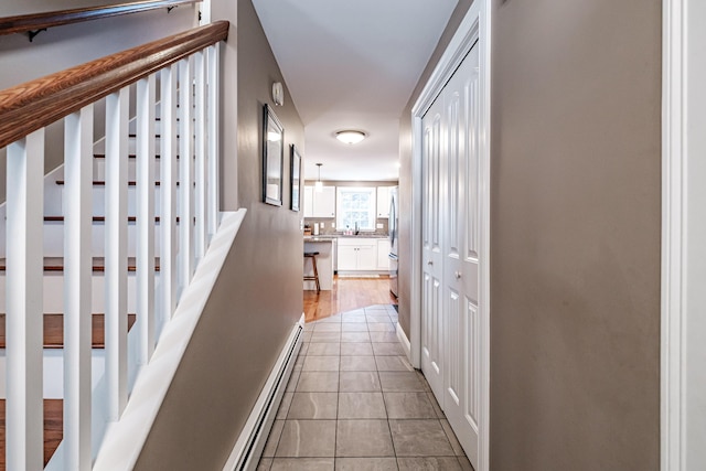 hall with stairs, baseboard heating, a sink, and light tile patterned flooring