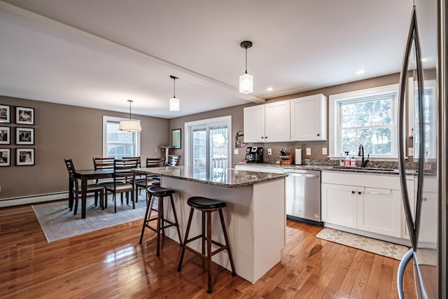 kitchen with stainless steel appliances, white cabinets, a sink, dark stone counters, and hardwood / wood-style floors