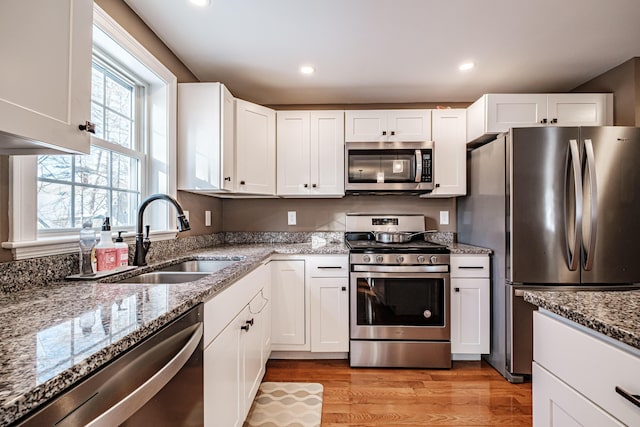 kitchen with white cabinets, stone countertops, stainless steel appliances, and a sink