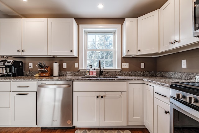 kitchen featuring recessed lighting, appliances with stainless steel finishes, white cabinetry, a sink, and dark stone counters