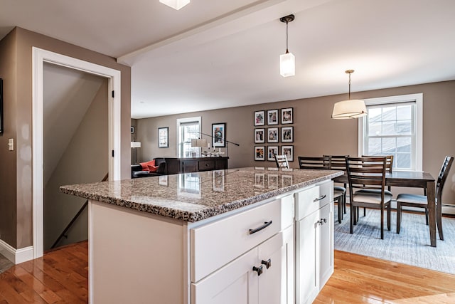 kitchen with light stone countertops, light wood-style floors, white cabinets, and a wealth of natural light