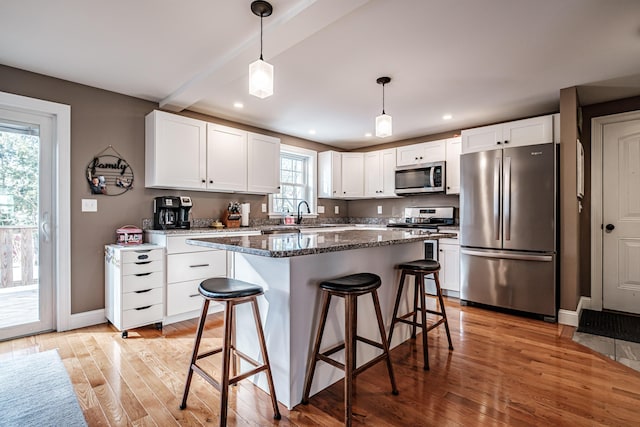 kitchen with light wood-style flooring, appliances with stainless steel finishes, white cabinetry, beamed ceiling, and a kitchen breakfast bar