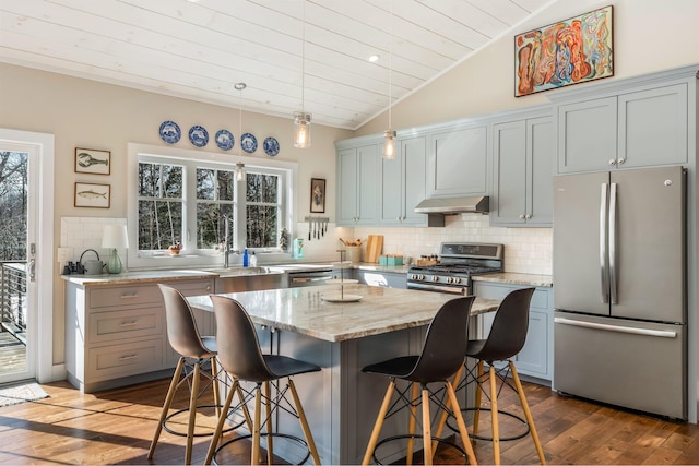 kitchen featuring tasteful backsplash, under cabinet range hood, lofted ceiling, a kitchen breakfast bar, and stainless steel appliances