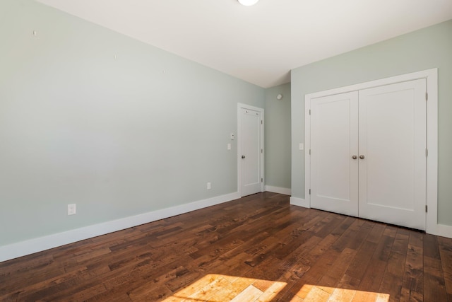 unfurnished bedroom with a closet, baseboards, and dark wood-style floors