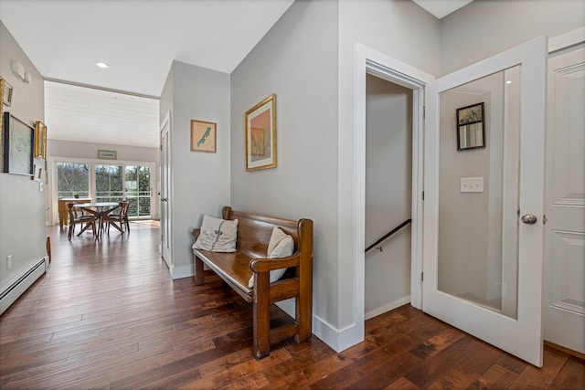 corridor featuring dark wood finished floors, baseboard heating, an upstairs landing, and baseboards