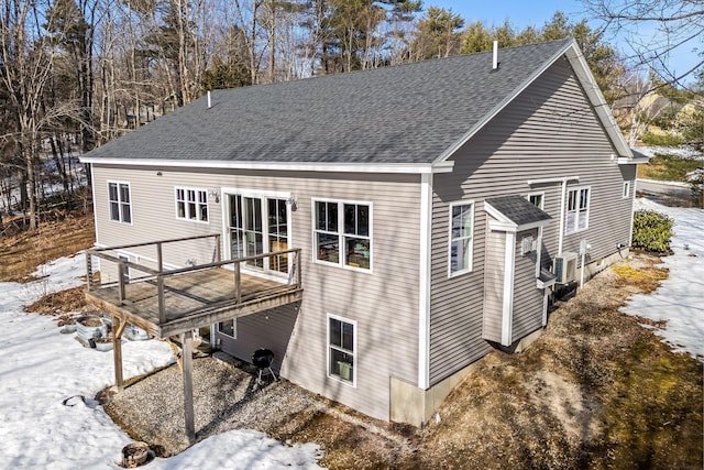 snow covered back of property with a wooden deck and roof with shingles