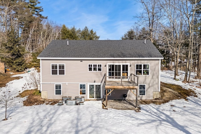 snow covered back of property with roof with shingles