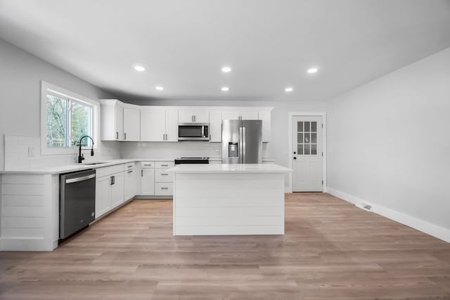 kitchen featuring a sink, appliances with stainless steel finishes, light wood-type flooring, a center island, and tasteful backsplash