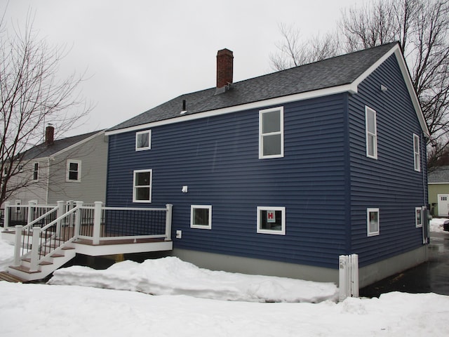 snow covered house featuring a chimney and a wooden deck