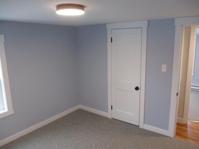 unfurnished room featuring baseboards, baseboard heating, and light colored carpet