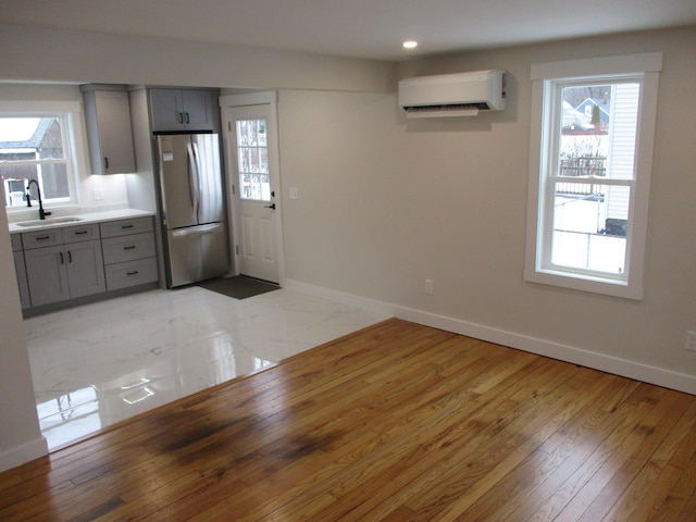 kitchen featuring baseboards, freestanding refrigerator, gray cabinetry, a sink, and a wall mounted AC