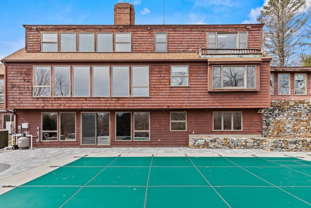 back of house featuring a patio, a shingled roof, a chimney, and a covered pool
