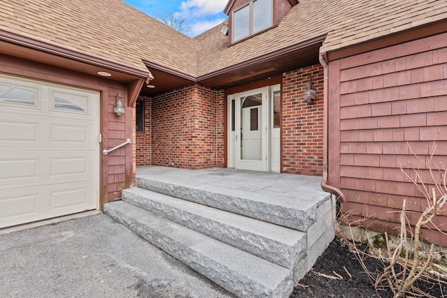entrance to property featuring brick siding, roof with shingles, and driveway