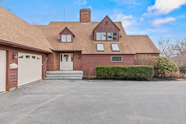 tudor-style house with a chimney, driveway, and a shingled roof