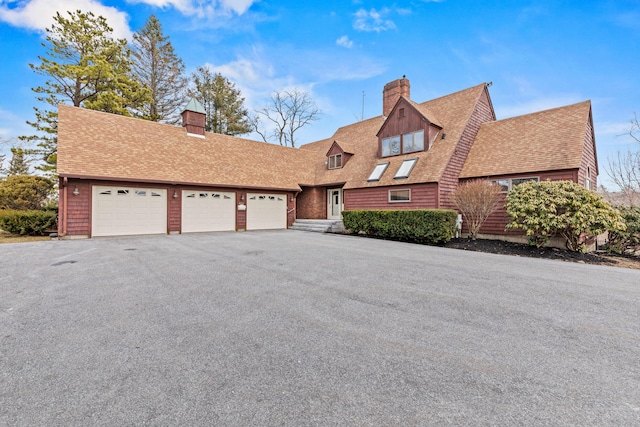 view of front of house with driveway, a chimney, roof with shingles, and a garage
