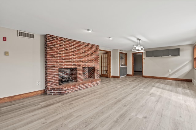 unfurnished living room with a fireplace, baseboards, visible vents, and light wood-style flooring