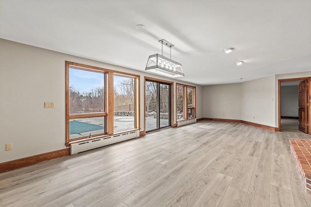 unfurnished living room with a baseboard heating unit, light wood-style floors, and plenty of natural light