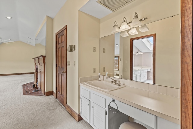 bathroom featuring vaulted ceiling, vanity, a fireplace, baseboards, and visible vents