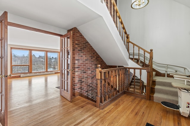 stairway with a baseboard heating unit, vaulted ceiling, wood finished floors, and french doors
