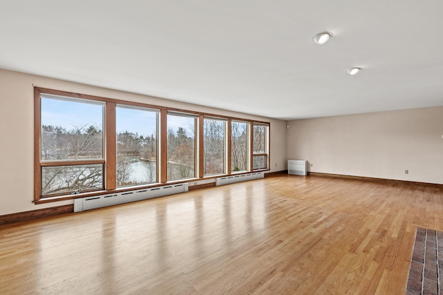 unfurnished living room featuring baseboard heating, baseboards, a healthy amount of sunlight, and wood finished floors