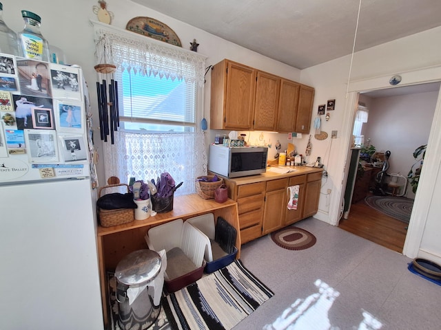 kitchen with brown cabinetry, light countertops, stainless steel microwave, and freestanding refrigerator