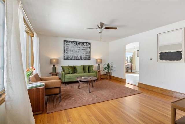 living area with a ceiling fan, baseboards, arched walkways, and wood finished floors