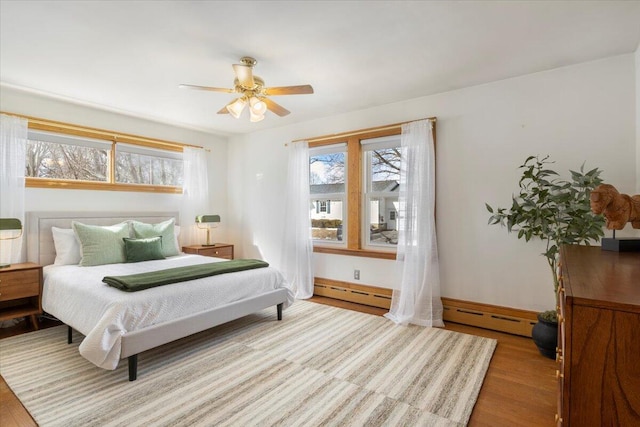 bedroom with multiple windows, baseboard heating, wood finished floors, and a ceiling fan