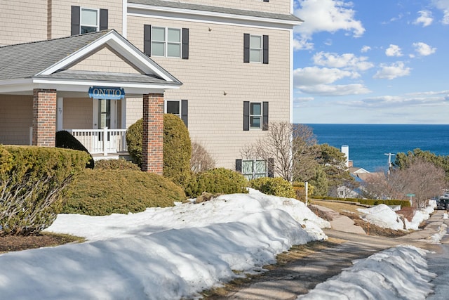 exterior space featuring a water view, a shingled roof, and a porch