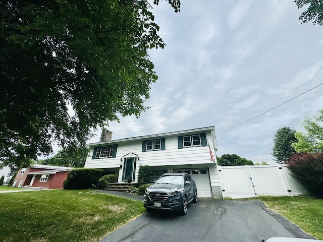 split foyer home with aphalt driveway, fence, a gate, a front lawn, and a chimney