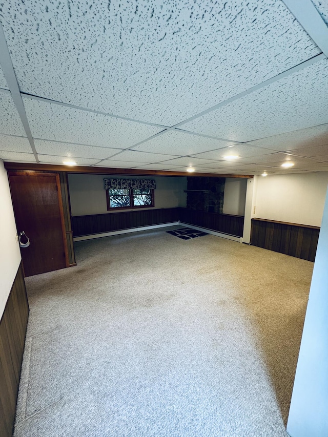 finished below grade area featuring carpet floors, a wainscoted wall, and a drop ceiling