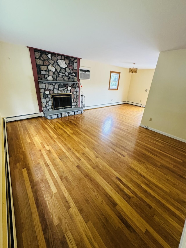 unfurnished living room with baseboards, a wall unit AC, wood finished floors, an inviting chandelier, and a stone fireplace