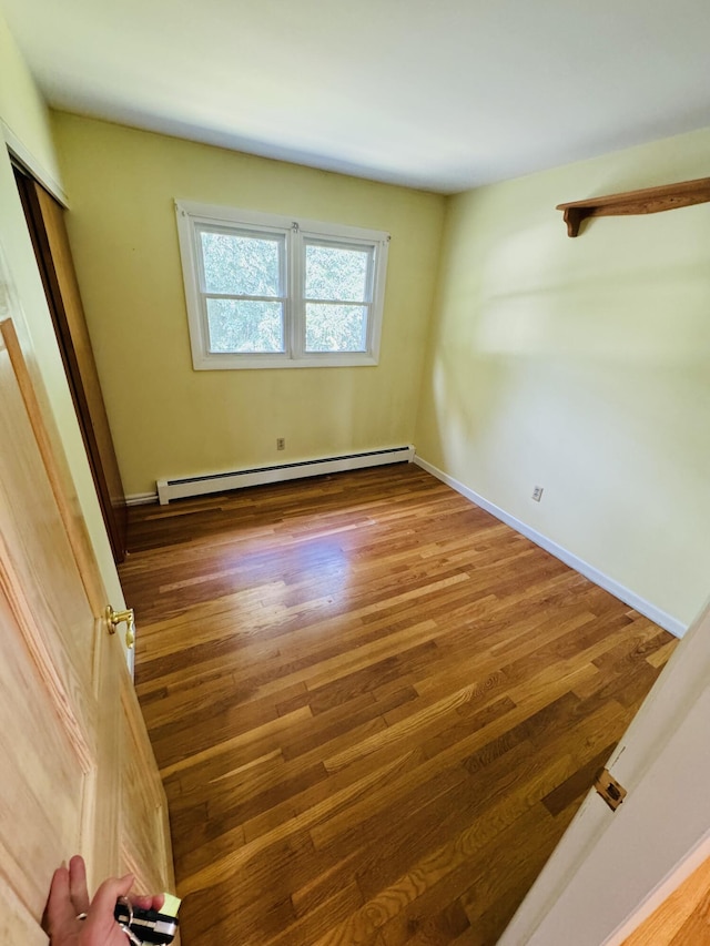 spare room featuring a baseboard heating unit, wood finished floors, and baseboards