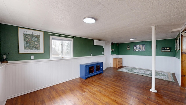 below grade area featuring a wall mounted air conditioner, wainscoting, and wood finished floors
