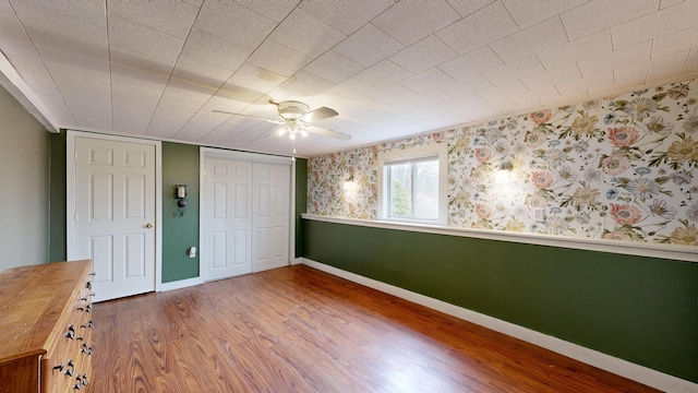 unfurnished bedroom featuring a closet, baseboards, wallpapered walls, ceiling fan, and wood finished floors
